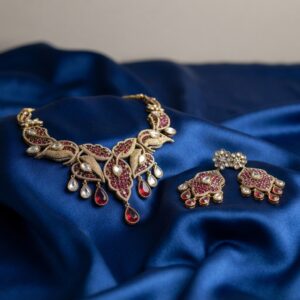 Antique gold-tone ruby red Indian necklace set with leaf design, teardrop drops and matching drop earrings on royal blue fabric