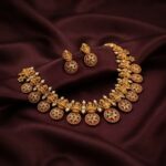Antique gold-tone Lakshmi necklace set with floral medallions, ruby-coloured stones and matching stud earrings on burgundy fabric