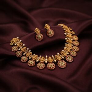Antique gold-tone Lakshmi necklace set with floral medallions, ruby-coloured stones and matching stud earrings on burgundy fabric
