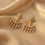 Gold-tone ear jacket earrings with cubic zirconia flower studs and fringe drops on beige fabric