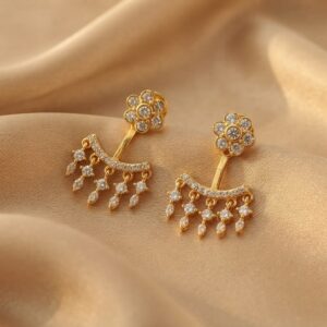 Gold-tone ear jacket earrings with cubic zirconia flower studs and fringe drops on beige fabric