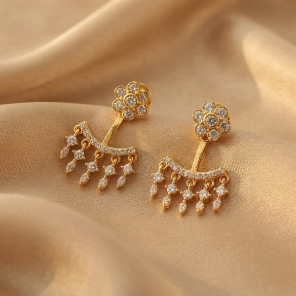 Gold-tone ear jacket earrings with cubic zirconia flower studs and fringe drops on beige fabric