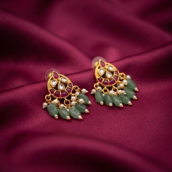 Antique gold-tone sage green earrings with ruby-coloured crescent stud, green bead fringe and faux pearl drops on burgundy fabric
