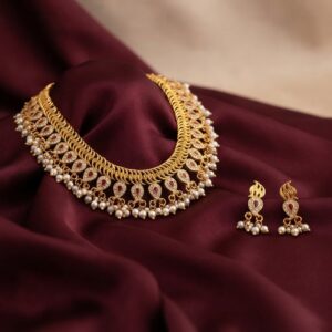 Gold-tone faux pearl necklace set with collar-style coiled band, ruby-coloured teardrop motifs and matching drop earrings on burgundy fabric