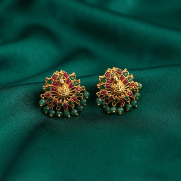 Antique gold-tone peacock stud earrings with ruby-coloured and green stones and green bead drops on green fabric