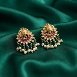 Antique gold-tone Ganesha stud earrings with ruby-coloured crescent, green beads and faux pearl drops on green fabric