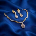 Gold-tone teardrop necklace set with cubic zirconia, blush-pink centre stones and matching drop earrings on royal blue fabric