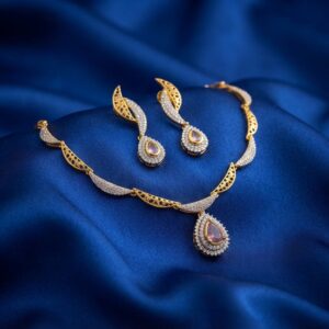 Gold-tone teardrop necklace set with cubic zirconia, blush-pink centre stones and matching drop earrings on royal blue fabric