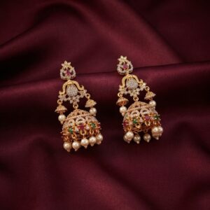 Gold-tone cubic zirconia jhumka earrings with ruby-coloured and green stones, side bells and faux pearl drops on burgundy fabric