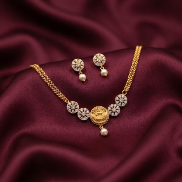 Gold-tone dainty necklace set with Lakshmi coin pendant, cubic zirconia flower medallions, faux pearl drop and matching stud earrings on burgundy fabric
