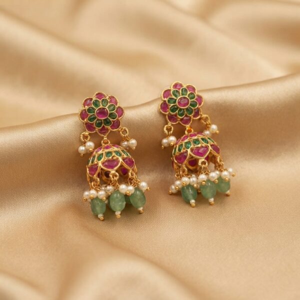 Antique gold-tone mini jhumka earrings with floral stud tops, ruby-coloured and green stones, green bead drops and faux pearls on champagne fabric