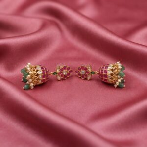 Antique gold-tone ruby red jhumka earrings with floral stud tops, lattice bells, green beads and faux pearl drops on dusty rose fabric
