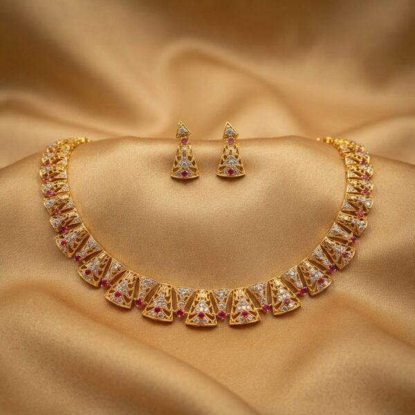 Gold-tone openwork wedding guest necklace set with cubic zirconia, ruby-coloured accents and matching triangular drop earrings on gold fabric