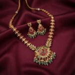Gold-tone mint green necklace set with ruby-coloured stones, bead drops, faux pearl accents and matching chandelier earrings on burgundy fabric