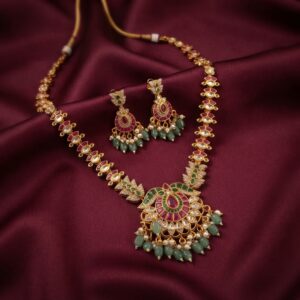 Gold-tone mint green necklace set with ruby-coloured stones, bead drops, faux pearl accents and matching chandelier earrings on burgundy fabric