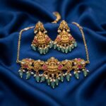 Antique gold-tone Lakshmi pendant necklace set with pink stones, green bead drops, faux pearl accents and matching chandelier earrings on royal blue fabric