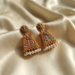Antique gold-tone gopuram earrings with Lakshmi stud tops, coral red and turquoise colour detail and faux pearl drops on cream fabric