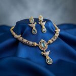 Gold-tone aqua blue necklace set with cubic zirconia, bird motif drop, aqua-coloured stones and matching drop earrings on royal blue fabric