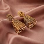 Antique gold-tone Lakshmi temple earrings with seated Lakshmi stud tops, carved tower drops and faux pearl fringe on dusty rose fabric