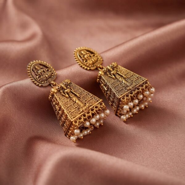 Antique gold-tone Lakshmi temple earrings with seated Lakshmi stud tops, carved tower drops and faux pearl fringe on dusty rose fabric