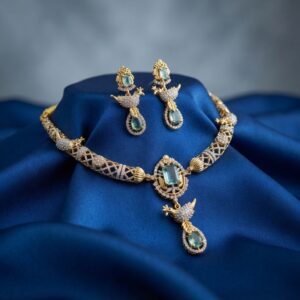 Gold-tone aqua blue necklace set with cubic zirconia, bird motif drop, aqua-coloured stones and matching drop earrings on royal blue fabric