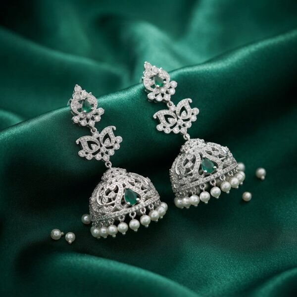 Silver-tone jhumka earrings with cubic zirconia, green teardrop stones and faux pearl drops on green fabric