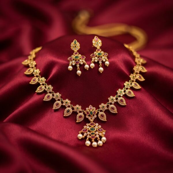 Gold-tone red and green necklace set with ruby-coloured and green stones, floral motifs, faux pearl drops and matching drop earrings on red fabric