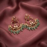 Antique gold-tone lotus earrings with ruby-coloured crescent, green bead fringe and faux pearl drops on dusty rose fabric