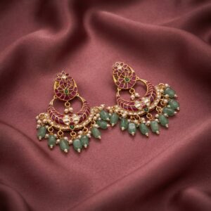 Antique gold-tone lotus earrings with ruby-coloured crescent, green bead fringe and faux pearl drops on dusty rose fabric
