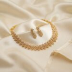 Gold-tone leaf necklace set with openwork leaf links, cubic zirconia and matching drop earrings on cream fabric