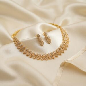 Gold-tone leaf necklace set with openwork leaf links, cubic zirconia and matching drop earrings on cream fabric