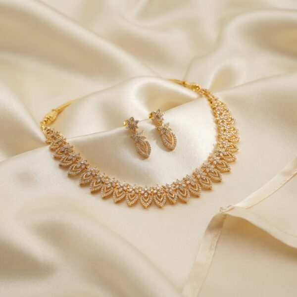 Gold-tone leaf necklace set with openwork leaf links, cubic zirconia and matching drop earrings on cream fabric