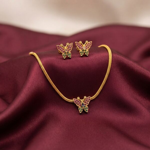 Gold-tone butterfly necklace set with pink and green stone-set butterfly pendant, woven chain and matching butterfly stud earrings on burgundy fabric