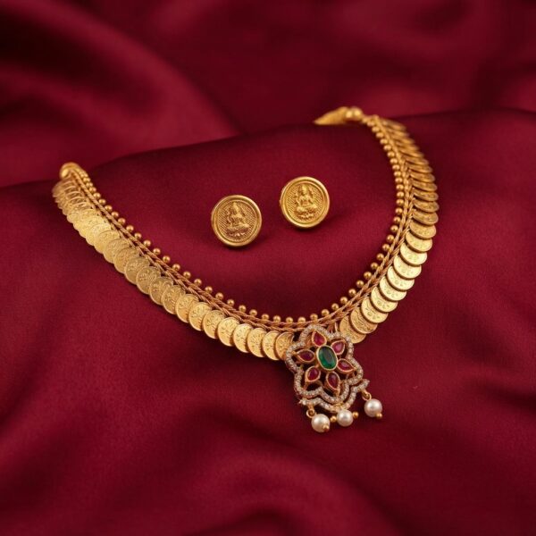 Gold-tone kasu mala Lakshmi coin necklace set with floral pendant, pearl-effect drops and matching coin stud earrings on maroon fabric