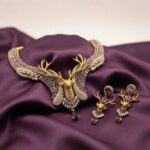 Gold-tone stag necklace set with antler centrepiece, lilac and clear stones and matching stag drop earrings on purple fabric