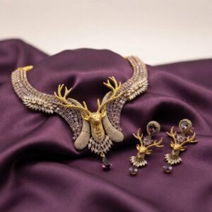 Gold-tone stag necklace set with antler centrepiece, lilac and clear stones and matching stag drop earrings on purple fabric