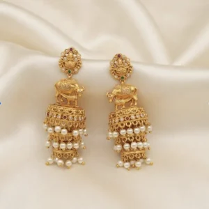 Antique gold-tone temple jhumka earrings with Lakshmi stud tops, cow motif, three-tier bells and faux pearl drops on cream fabric