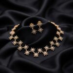 Gold-tone star necklace set with linked cubic zirconia starburst motifs and matching drop earrings on black fabric