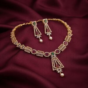Gold-tone art deco necklace set with cubic zirconia, ruby-coloured stones, faux pearl drop and matching drop earrings on burgundy fabric