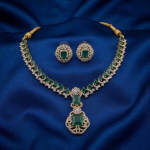 Gold-tone American diamond necklace set with emerald-coloured stones, cubic zirconia detailing and matching stud earrings on navy blue fabric