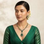 Gold-tone American diamond necklace set with emerald-coloured stones, cubic zirconia detailing and matching stud earrings on navy blue fabric