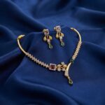 Gold-tone hasli necklace set with rigid collar, cubic zirconia, ruby-coloured and green stones and matching drop earrings on royal blue fabric