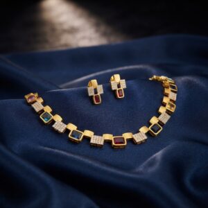 Modern gold-tone square link necklace set with cubic zirconia, coloured emerald-cut stones and matching drop earrings on navy fabric