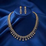 Gold-tone fringe long necklace set with cubic zirconia loop motifs, flower charm drops and matching drop earrings on royal blue fabric