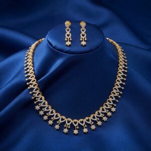 Gold-tone fringe long necklace set with cubic zirconia loop motifs, flower charm drops and matching drop earrings on royal blue fabric