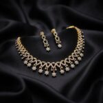Gold-tone fringe necklace set with cubic zirconia loop motifs, flower charm drops and matching drop earrings on black fabric