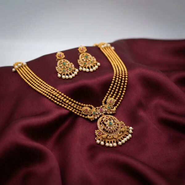 Antique gold-tone multi-strand bead temple jewellery necklace set with ornate pendant, pearl-effect drops and matching chandelier earrings on maroon fabric